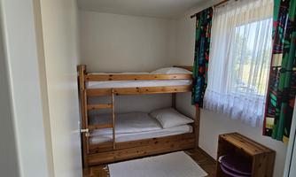 A bright room with a colorful curtain and a wooden bunk bed. There is a small table and a carpet on the floor.