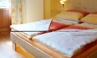 A cozy bedroom with a large double bed and warm blankets. Soft light brightens the room, which is furnished with a table and chairs as well as an armchair.