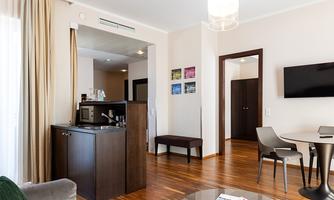 A modern hotel room with wooden floors and bright walls. There is a table, chairs, and a small kitchenette.
