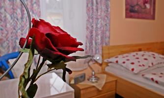A cozy bedroom with a bed and beautiful, colorful curtains. In the foreground, there is a red rose in a vase.