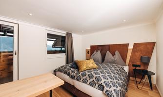 A modern bedroom with a large bed and beautiful bedding. There is a small table and a window that lets in light.