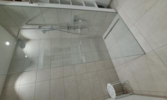 A modern shower with a glass wall and a rainforest showerhead. The space is simply tiled and well lit.