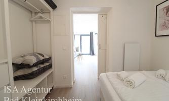 A bright bedroom with a large bed and a wardrobe. The room has access to another area with large windows.