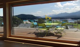 A beautifully designed balcony with a table and colorful chairs. In the background, mountains and a clear sky are visible.