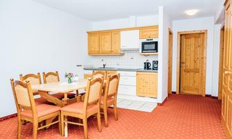 A bright kitchen with a dining table and six chairs. The wooden furniture and the red carpet give the room a cozy atmosphere.
