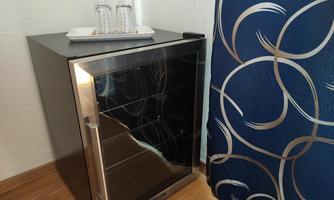 A small refrigerator stands in a corner, on a tray there are two glasses. In the background, you can see a blue curtain with a pattern.