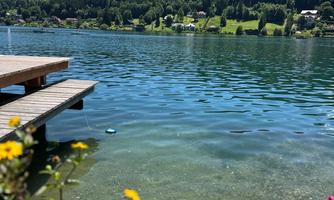 A beautiful lake with clear, blue water and a picturesque landscape in the background. Colorful flower frames around the wooden dock create an inviting atmosphere.