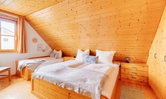 A cozy bedroom with slanted walls and wooden furniture. Two beds with white pillows and a warm atmosphere.