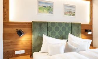 A stylish bedroom with a cozy double bed and a green headboard wall. Two picture frames on the wall and soft lighting create an inviting atmosphere.