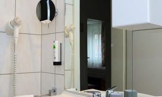 A modernly furnished bathroom with a sink, mirror, and towels. The room is bright and clean, with white tiles on the walls.