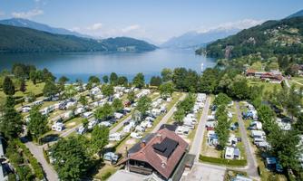 A beautiful campsite by the lake with many campervans. In the background, mountains and trees can be seen.
