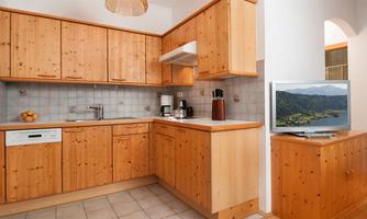 A modern kitchen with wooden cabinets and stylish design. A television and a fruit bowl are important for coziness.