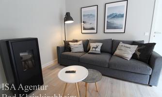 A cozy living room with a gray sofa and decorative pillows. Next to the sofa is a small table and a floor lamp.