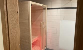 A modern wooden sauna with glass doors. The interior lighting is in soft red.