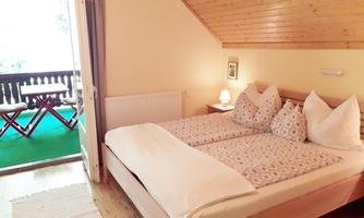 A cozy bedroom with a double bed and wooden walls. The balcony is visible and offers a relaxing view.