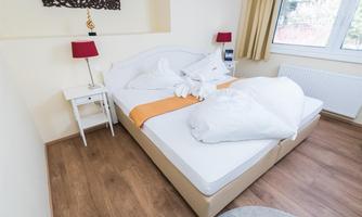 A cozy bedroom with a double bed and two red lamps. The room has a bright, welcoming atmosphere and a large window front.