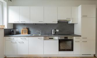 A modern kitchen with white cabinets and gray walls. It includes appliances such as a stove, a refrigerator, and a sink.