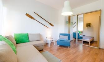 A modern living room with a bright sofa and a blue armchair. Oars are hanging on the wall and a mirror is visible.