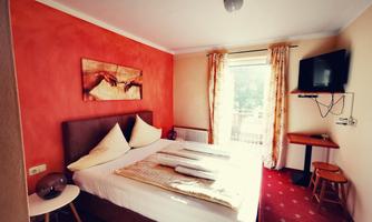 A cozy bedroom with a double bed and decorative pillows. The walls are painted in warm colors, and there is a television as well as a small table.