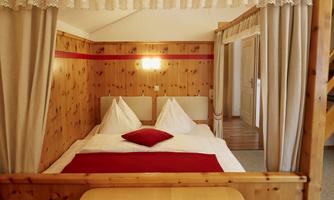 A cozy bedroom with wooden interiors. The bed has white bedding and red accents.