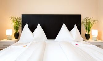 A cozy bedroom with two beds and white bedding. There are plants and lamps on the nightstands.