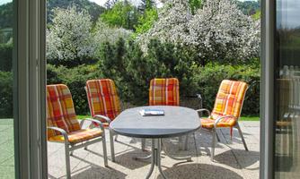An inviting outdoor area with a round table and four chairs. In the background, the trees are blooming, and nature is green and vibrant.