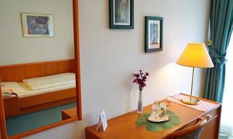 A cozy room with a desk and a chair. In the background, there is a bed and a mirror visible.