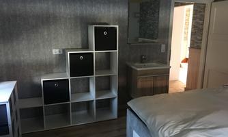 A modern bedroom with a bed, a shelf, and a sink. The walls are painted in a neutral tone.