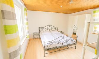 A bright bedroom with a double bed and a wardrobe. The windows are decorated with modern curtains.