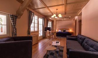 A cozy vacation apartment with wooden floors and warm colors. It features a double bed, a seating area, and large windows for plenty of light.