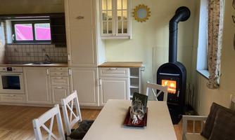 A cozy kitchen with a wood stove and a dining table. The room has bright walls and friendly light.