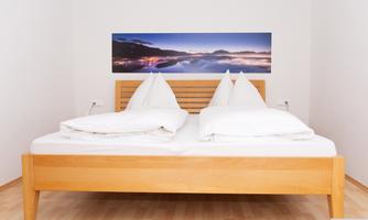 A simple bedroom with a wooden double bed. A picture of a scenic view hangs on the wall.