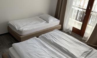 A simple, bright room with two single beds and a double bed. A balcony with a window and a television on the wall complete the ambiance.
