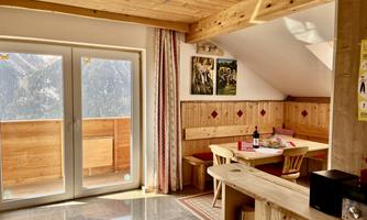 A cozy living space with wooden furniture and a dining table. Large windows offer a view of the mountains.