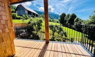 A beautiful view from a balcony over a green landscape with hills and trees. In the background, a traditional wooden house can be seen.