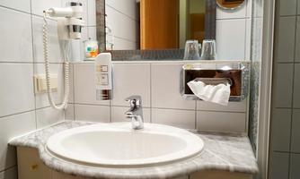 A modern bathroom with a marble sink and a large mirror. The walls are tiled, and there is a towel holder as well as glasses in an elegant holder.