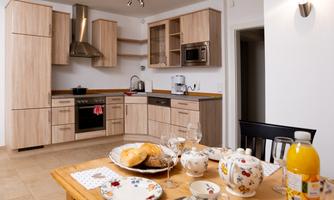 A modern kitchen with wooden cabinets and a stove. The table is festively set with dishes and fresh rolls.