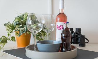 An elegant tray with a bottle of rosé wine, glasses, and a bowl. Next to it is a plant in a pot and a small glass bottle.