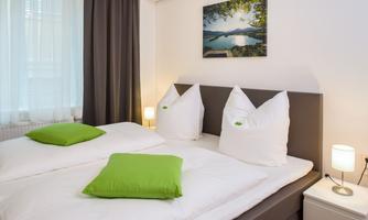 A modern bedroom with a double bed and green pillows. On the wall hangs a picture of a tranquil landscape.