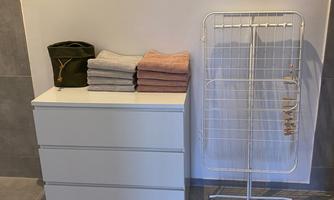 A bright room with a white dresser and folded towels. Next to it stands a drying rack.