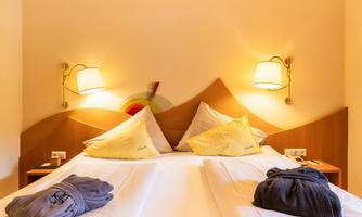 A cozy bedroom with a double bed and two pillows. The warm walls and lamps create a relaxed atmosphere.