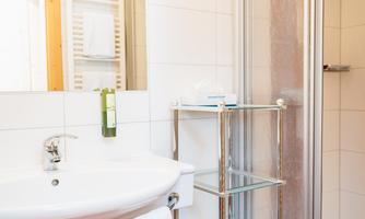 A modern bathroom with a sink, a shower cabin, and a shelf. The walls are brightly tiled and there are some towels.