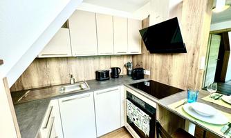 A modern kitchen with light cabinets and wooden legs. It is well equipped with a stove, a sink, and modern appliances.