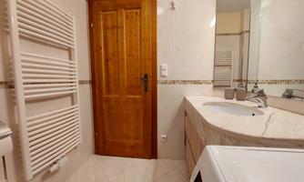 A modern bathroom with a wooden shelf and an elegant sink unit. The walls are light and the tiles are in neutral tones.