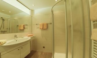 A modern bathroom with a shower cabin and a sink. The walls are light and the towels are in soft tones.