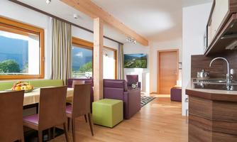 A bright and modern open kitchen with large windows. The room is equipped with a dining area and cozy seating.