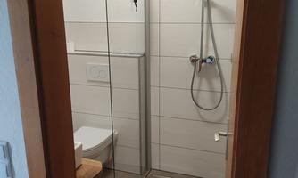 A modern bathroom with a glass shower cubicle and a toilet. The floor is tiled with neutral tiles and a towel is ready.