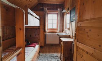 A cozy room with wood paneling and a bunk bed. A window provides daylight and there is a small dresser as well as a sink.