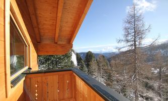 A balcony with wooden cladding and a view of snow-covered mountains. The sun is shining and the sky is clear.
