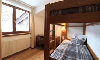 A cozy room with a loft bed and a desk. The window provides daylight and a view outside.